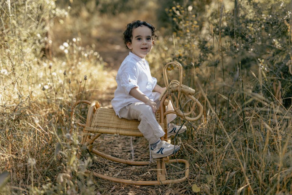ילד בן שלוש יושב על סוס נדנדה בשדה יבש