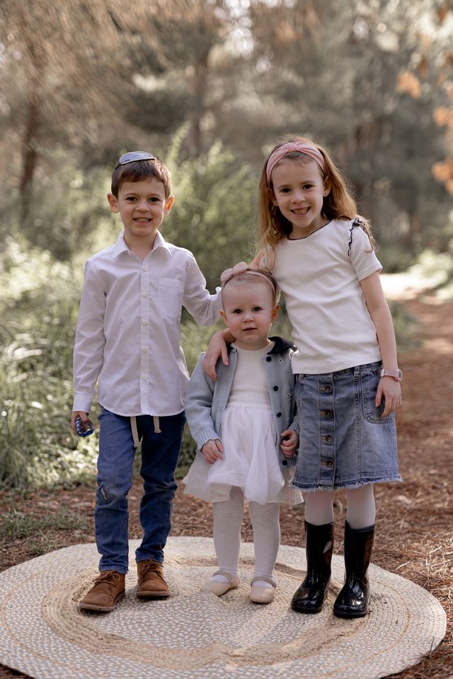שלושה ילדים מחייכים על במת עץ ביער
