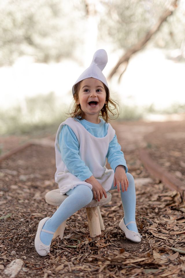 ילדה בתחפושת דרדסית לפורים יושבת ביער וצוחקת